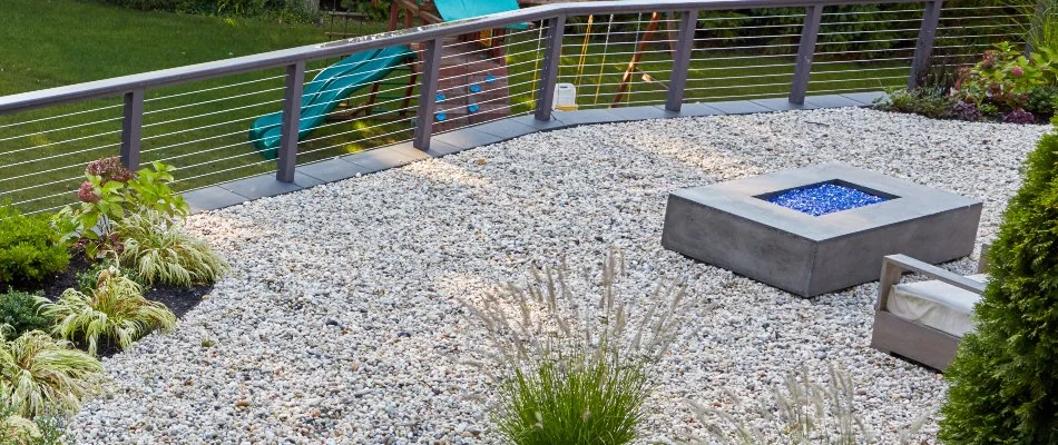 Modern fire pit on a gravel patio with a railing in White Plains, NY.