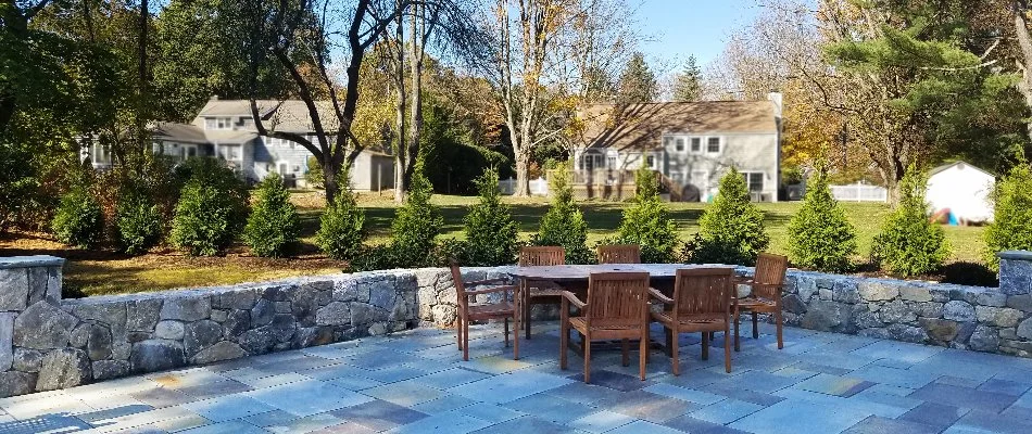 Patio in Greenwich, CT, with dining set near landscaping with small shrubs. 